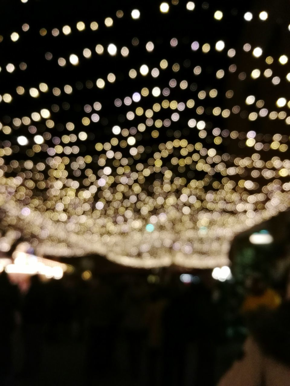 DEFOCUSED IMAGE OF ILLUMINATED CHRISTMAS LIGHTS AGAINST SKY AT NIGHT