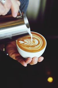 Cropped image of hand pouring milk into cappuccino