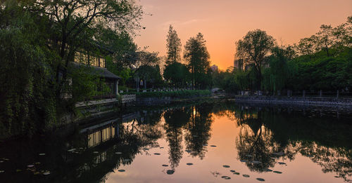 Reflection of silhouette trees in lake against sky during sunset