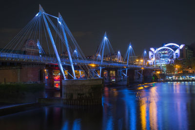 Illuminated bridge over river against sky at night