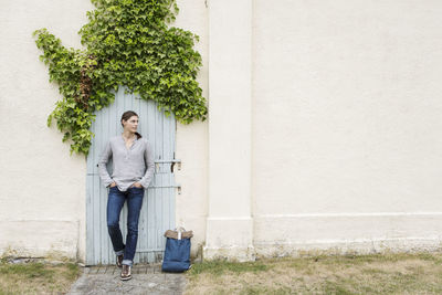 Thoughtful woman standing against closed door with ivy on house wall