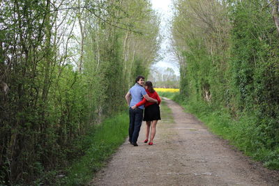 Rear view portrait of couple walking on road by plants
