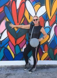 Portrait of woman wearing sunglasses standing against graffiti wall