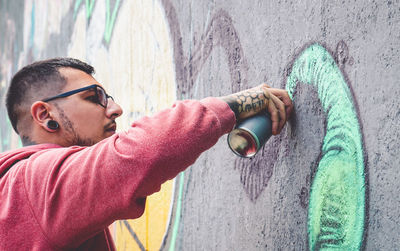 Side view of young man wearing sunglasses standing against wall