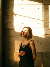 Young woman looking away while standing against wall