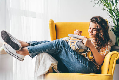 Young woman using mobile phone while sitting on sofa at home