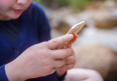 Midsection of woman using smart phone while sitting outdoors