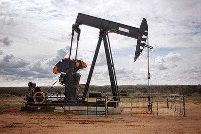 Oil rig on field against cloudy sky