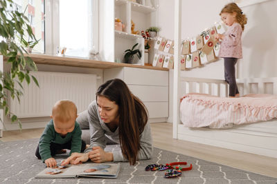 Mother spending time with two kids at home before christmas. looking photos in album, girl getting