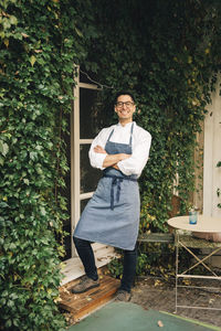 Happy male chef standing with arms crossed outside restaurant