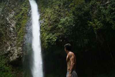 Shirtless man sitting in front of la fortuna waterfall in costa rica