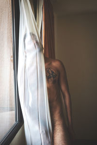 Close-up of shirtless man holding window at home