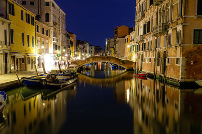 Boats moored in canal amidst buildings in city at night