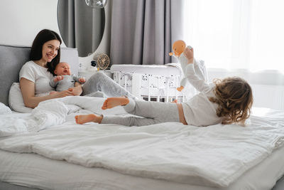 Mama with two kids at home in bedroom. baby infant resting on mothers hands, while older sister