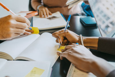 Hands of university students writing in book at cafeteria