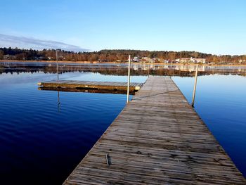 Wooden pier in lake against clear blue sky