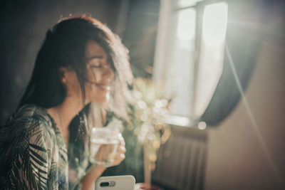 Young woman looking through window at home