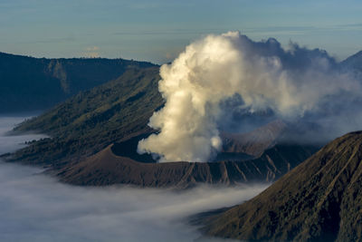 Aerial view of volcano emitting smoke against sky