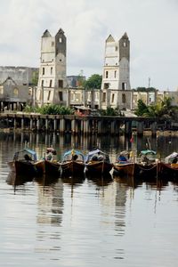 Boats moored in river against sky in city