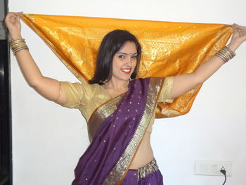 Portrait of smiling woman in sari standing against wall