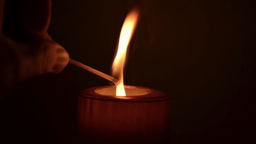 Close-up of hand holding illuminated matchstick over candle