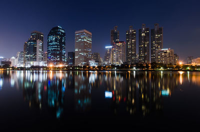 Illuminated buildings by river against sky at night