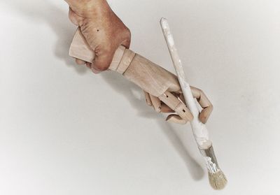 Cropped image of man holding wooden hand with brush against white background