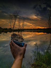 Optical illusion of hand holding rowboat in lake during sunset