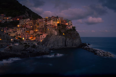 Illuminated buildings by sea against sky at dusk