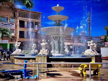 Fountain in city against blue sky