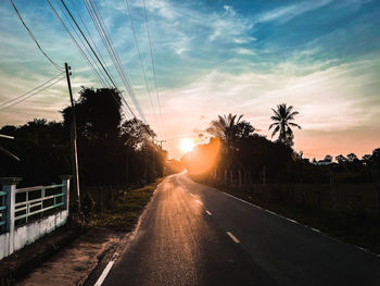 Road by trees against sky during sunset