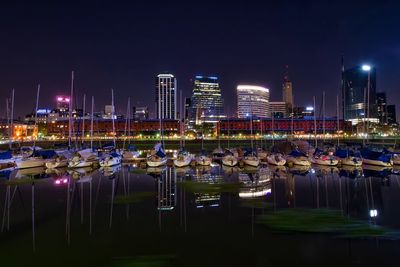 Boats moored on lake against city at night