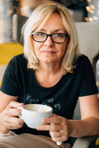 Mature woman holding coffee cup sitting at cafe