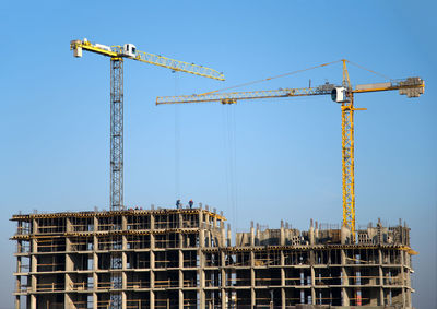 Low angle view of cranes at construction site against sky