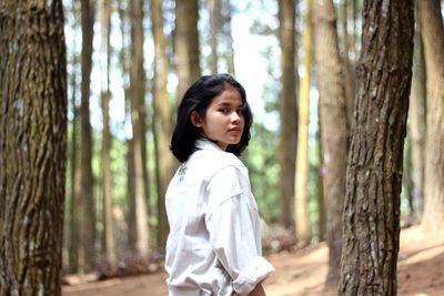 Side view of woman standing by tree trunk in forest