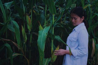 Side view of young woman standing by crops in farm