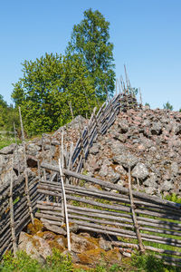 Stone wall by trees against clear blue sky