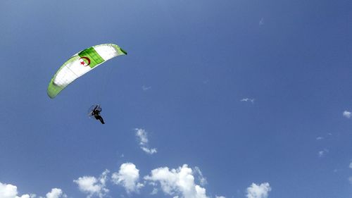 Low angle view of person powered paragliding against blue sky