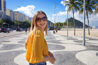 Portrait of smiling young woman walking along copacabana beach promenade, rio de janeiro, brazil. 