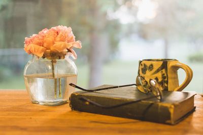 Close-up of eyeglasses on book by flower vase at table