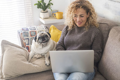 Smiling woman using laptop sitting with dog at home