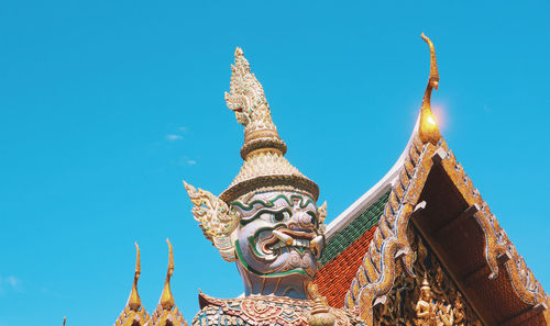 Low angle view of temple against building against clear blue sky and a demon statue in bangkok