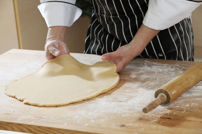 Midsection of chef rolling dough at table
