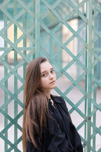 Portrait of young woman standing by metal grate outdoors