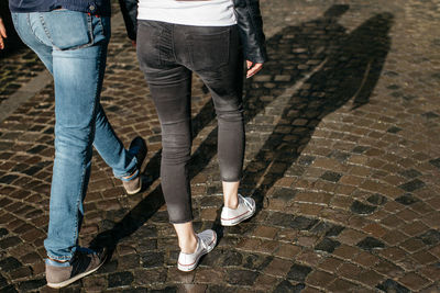 Low section of friends walking on cobblestoned footpath