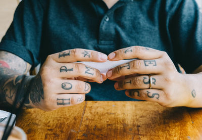 Midsection of man with tattooed hands holding paper on table