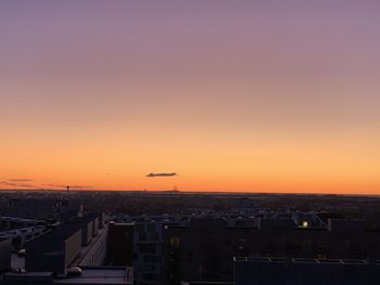 Airplane flying over buildings in city against sky during sunset