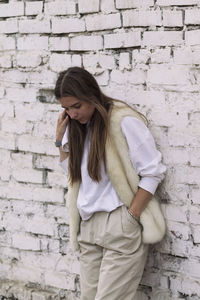 Young woman standing against brick wall