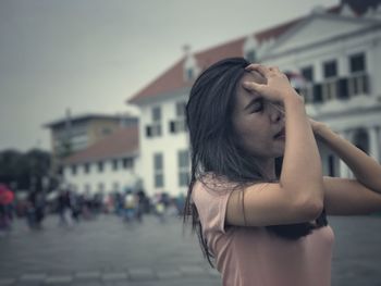 Woman with closed eyes adjusting hair against buildings in city