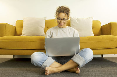 Front view of woman using laptop sitting by sofa